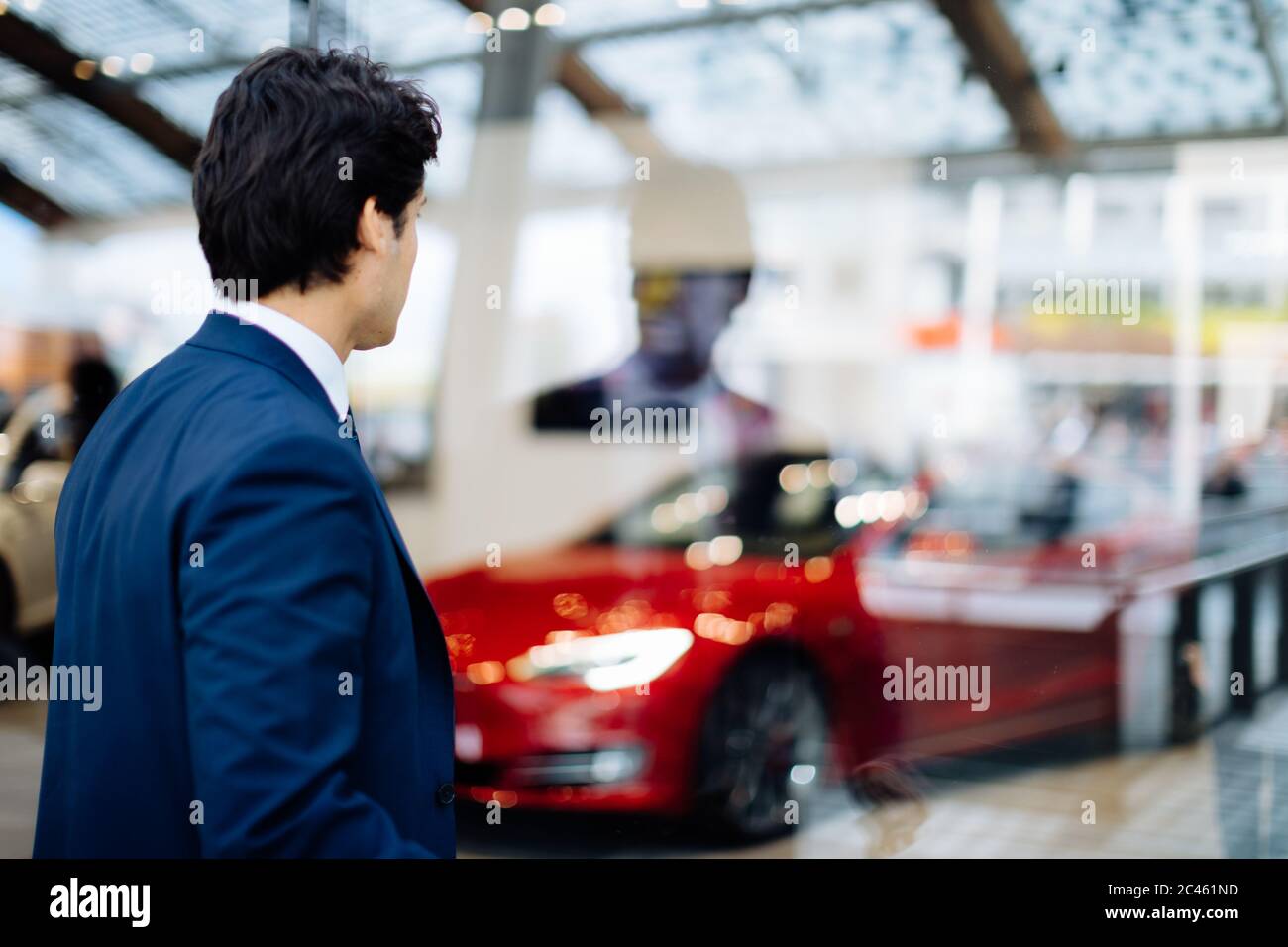 Businessman looking through glass wall at sports car in showroom Stock Photo