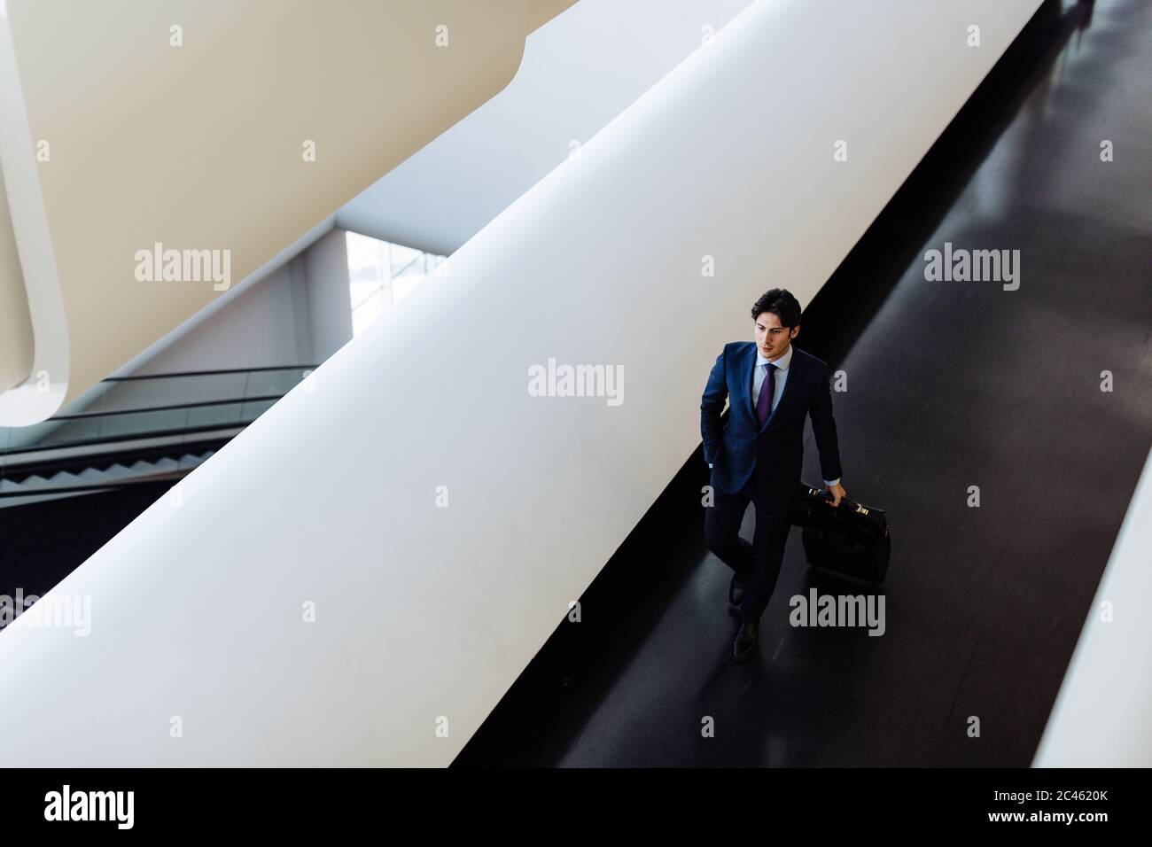 Businessman with wheeled luggage in hotel building Stock Photo