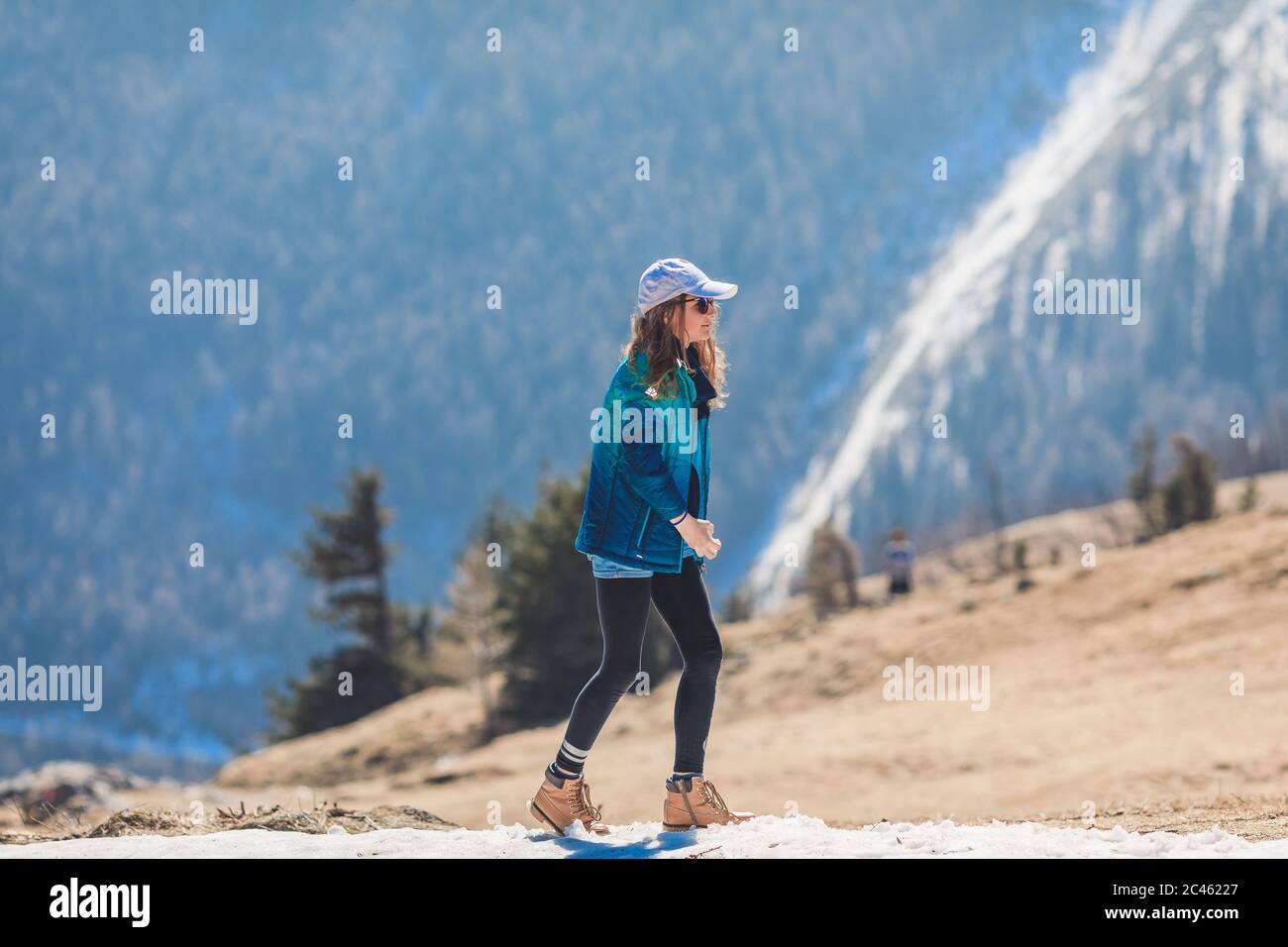 Young girl, tween age, wearing sun cap and sunglasses hiking through melting snow in alpine scenery Stock Photo