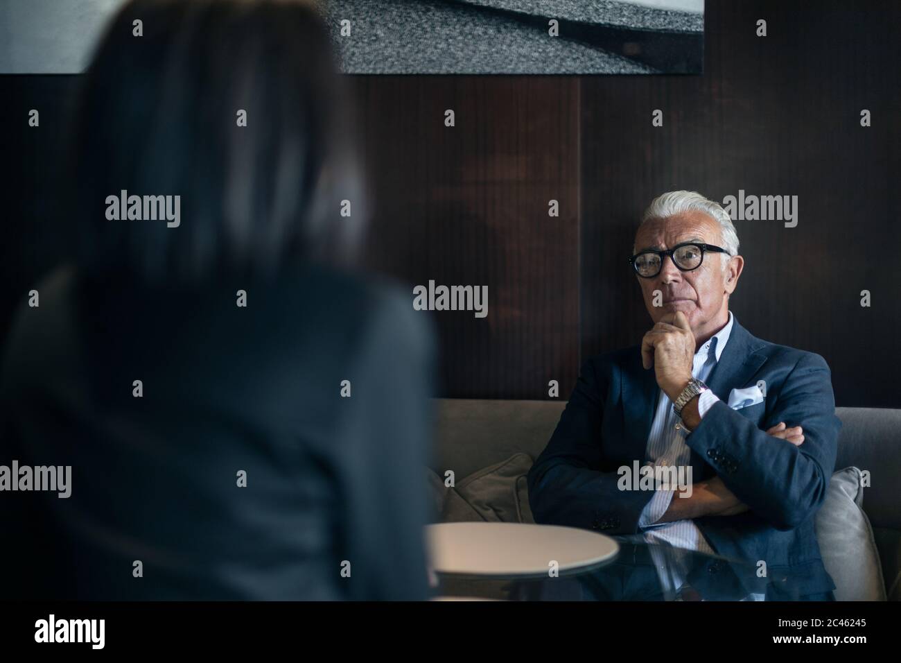 Senior businessman sitting in hotel table meeting with businesswoman, over shoulder view Stock Photo