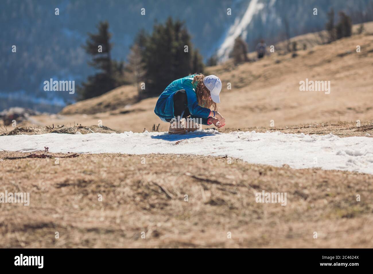 Young girl, tween age, wearing sun cap and sunglasses playing with melting snow in alpine scenery Stock Photo