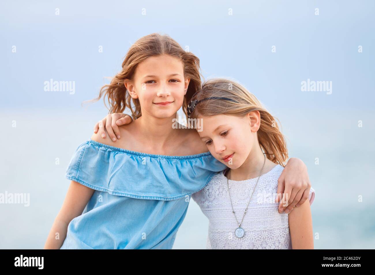 Two young girls wearing casual summer clothing looking, smiling at camera in a coastal region Stock Photo
