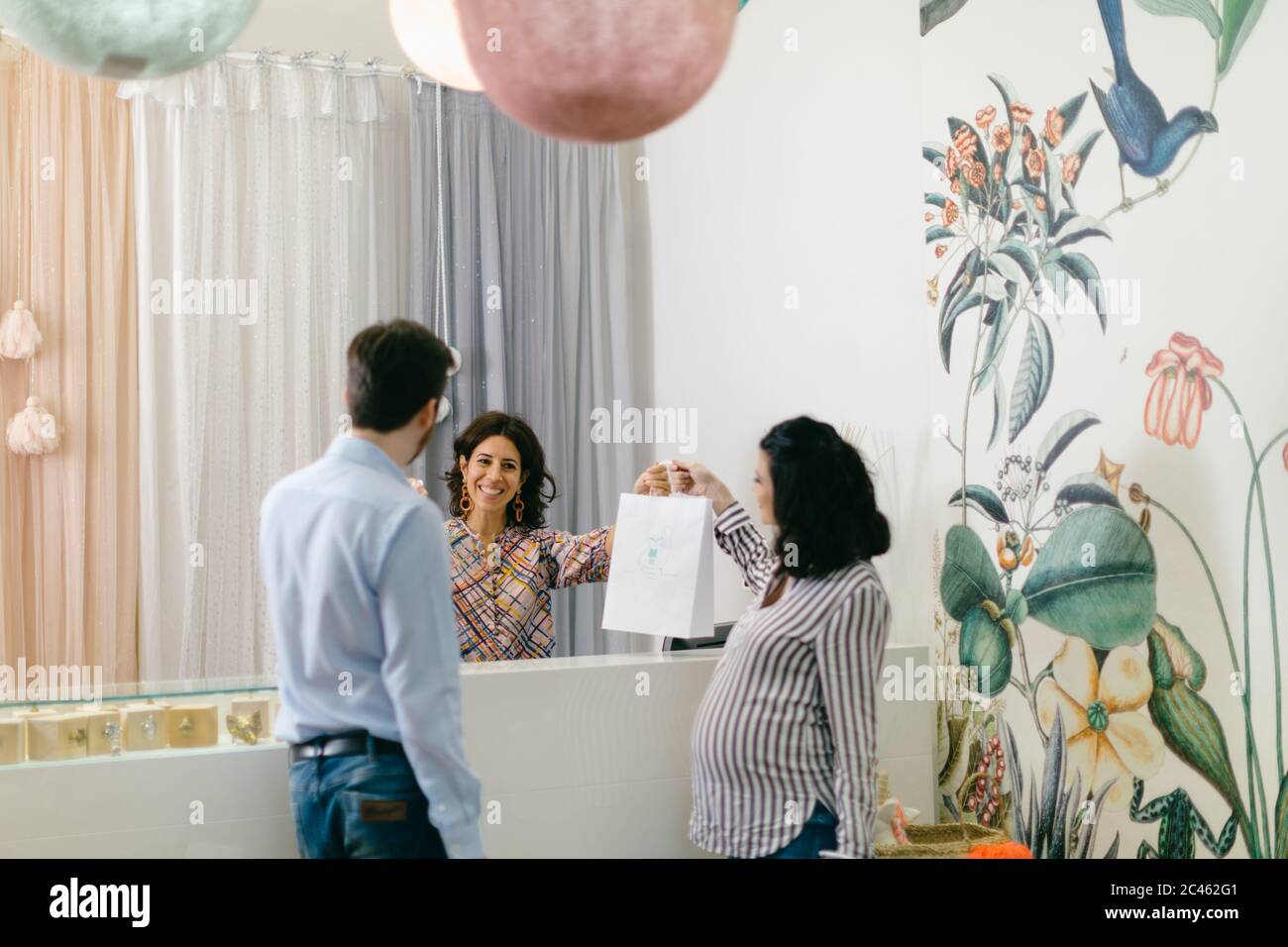 Shop keeper and pregnant couple at cash till Stock Photo