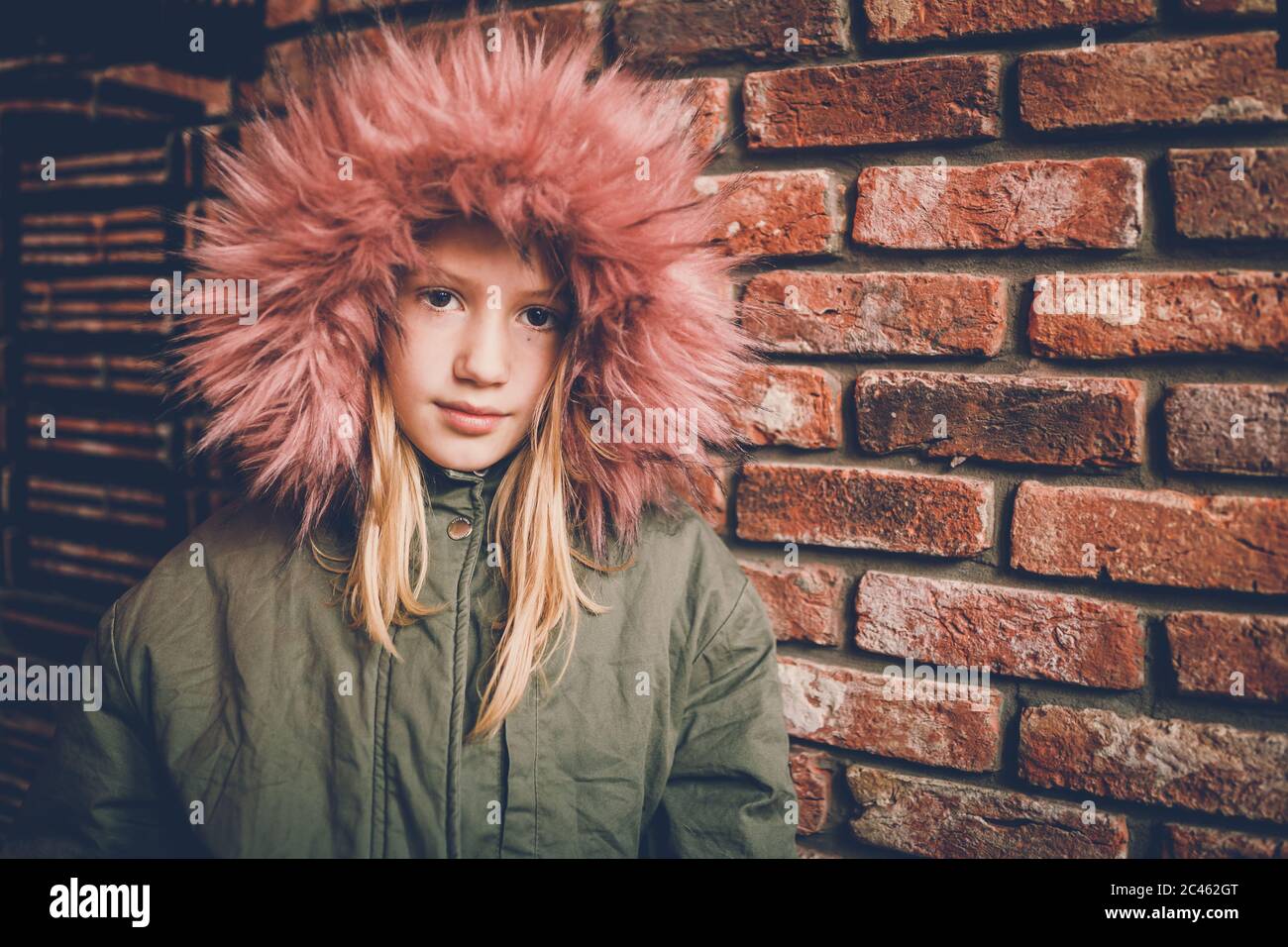 Young girl wearing fur jacket standing in front of brick wall and looking at camera Stock Photo
