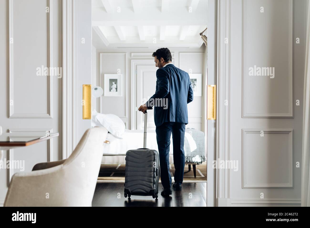 Businessman with wheeled luggage in suite Stock Photo