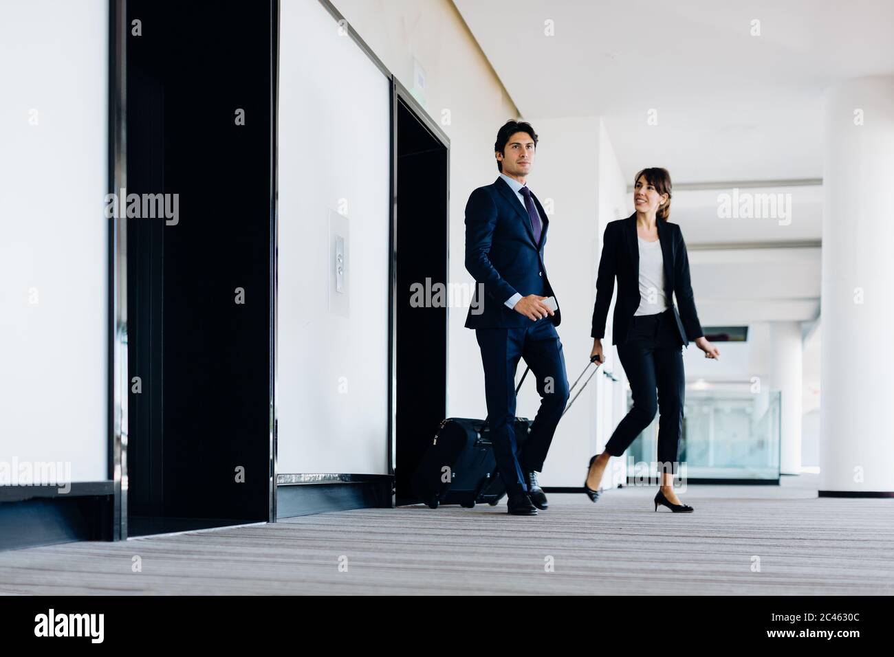 Businessman and businesswoman with wheeled luggage in hotel building Stock Photo