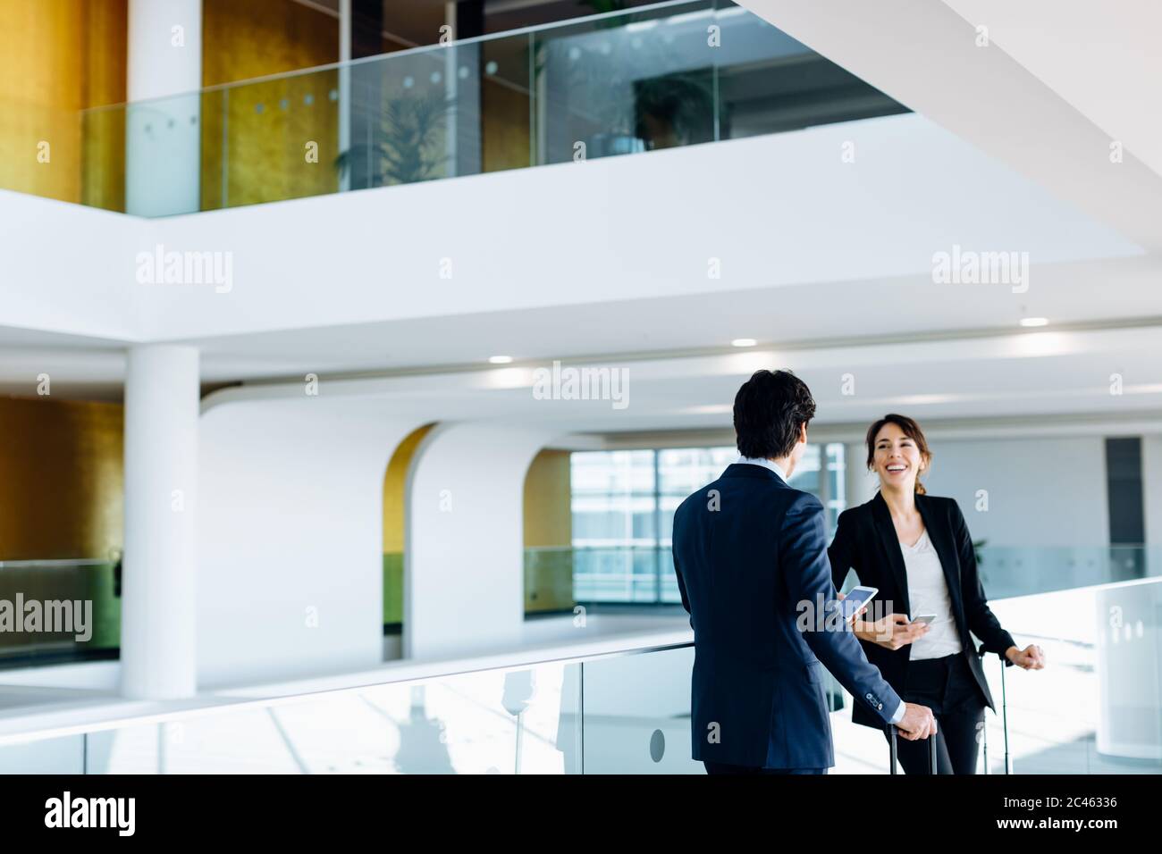 Businessman and businesswoman with wheeled luggage in hotel building Stock Photo