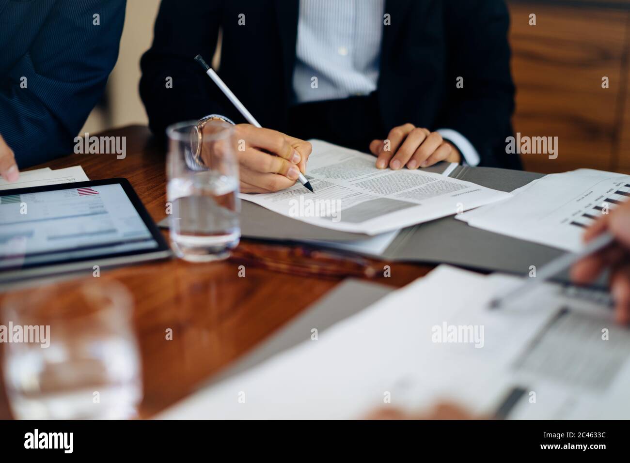 Businessmen and woman at boardroom table working on paperwork, cropped Stock Photo