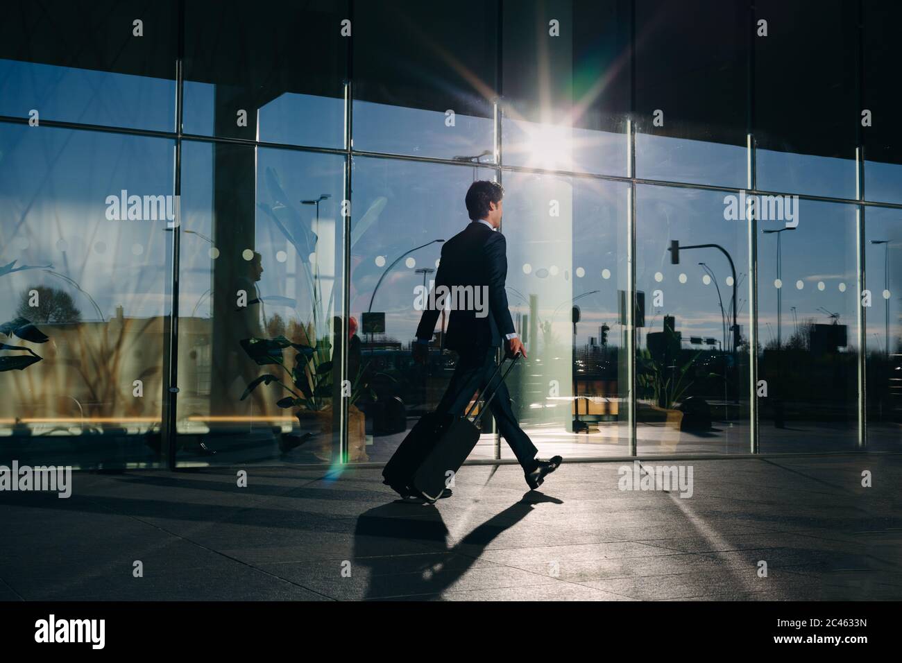 Businessman with wheeled luggage passing glass building, Malpensa, Milan Stock Photo
