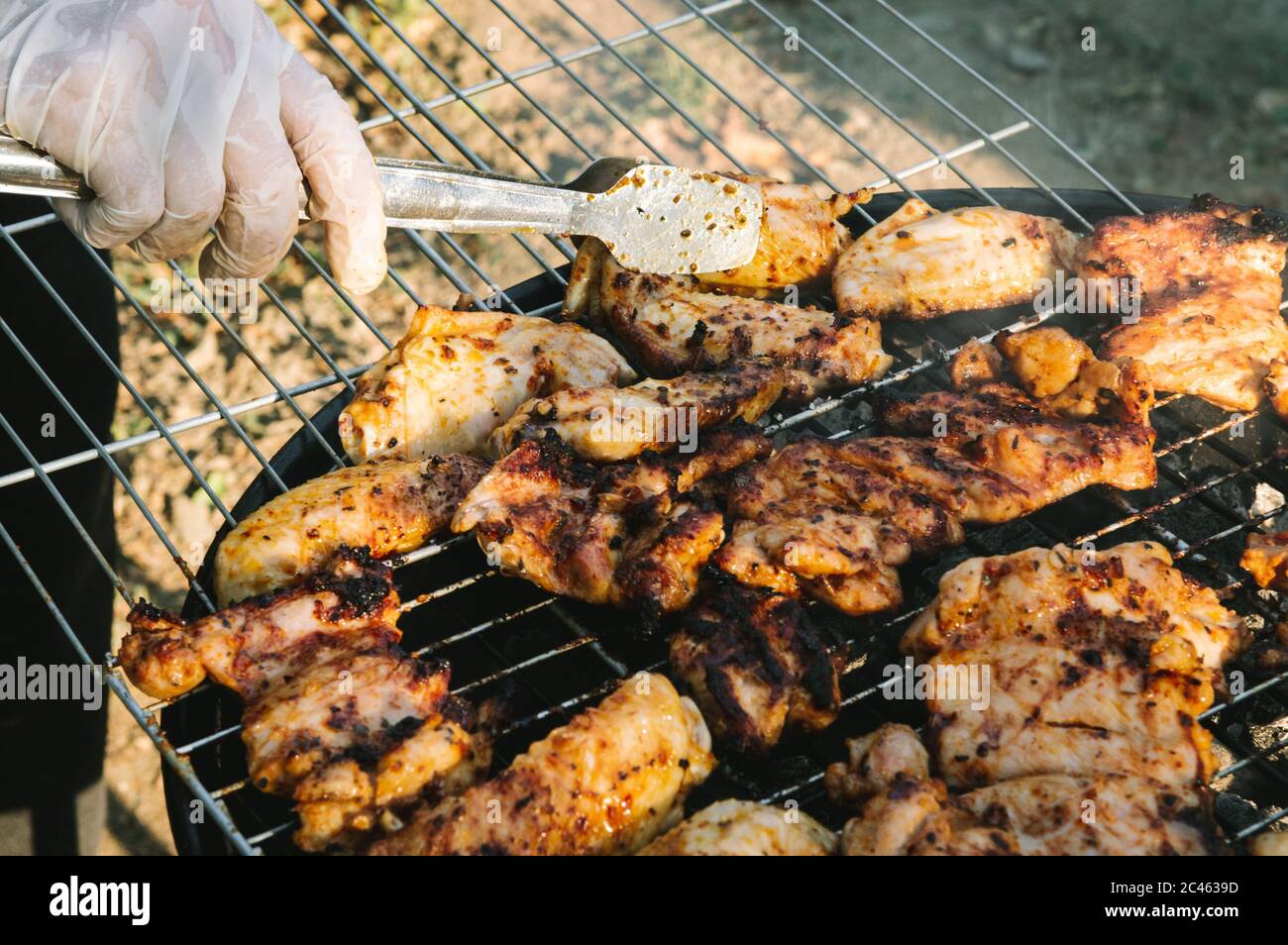 Flipping barbecued chicken meat with tongs on a charcoal barbeque grill. Tasty snack party. Stock Photo