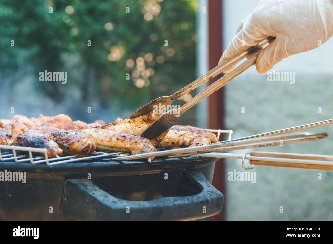 Flipping barbecued chicken meat with tongs on a charcoal barbeque grill. Tasty snack party. Stock Photo