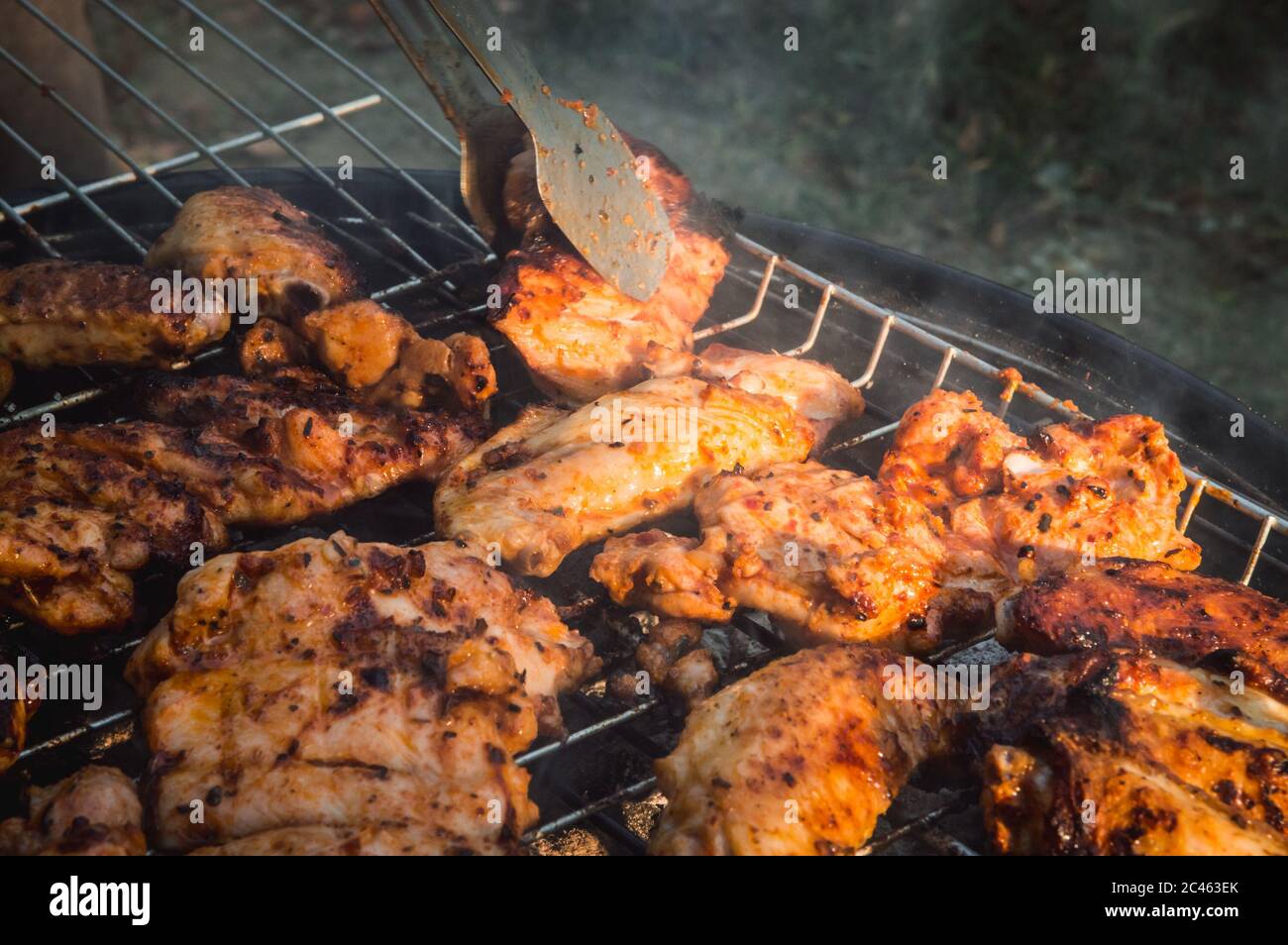 Flipping a barbecued chicken meat with tongs on a charcoal barbeque grill. Tasty snack party. Stock Photo