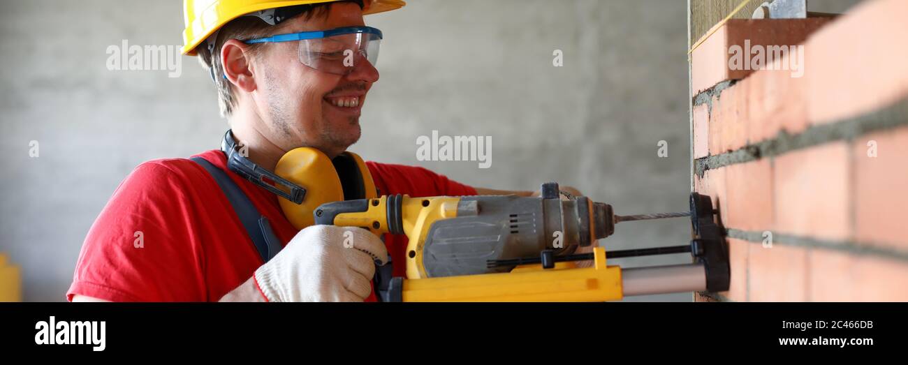 Builder drilling hole in wall, construction site Stock Photo