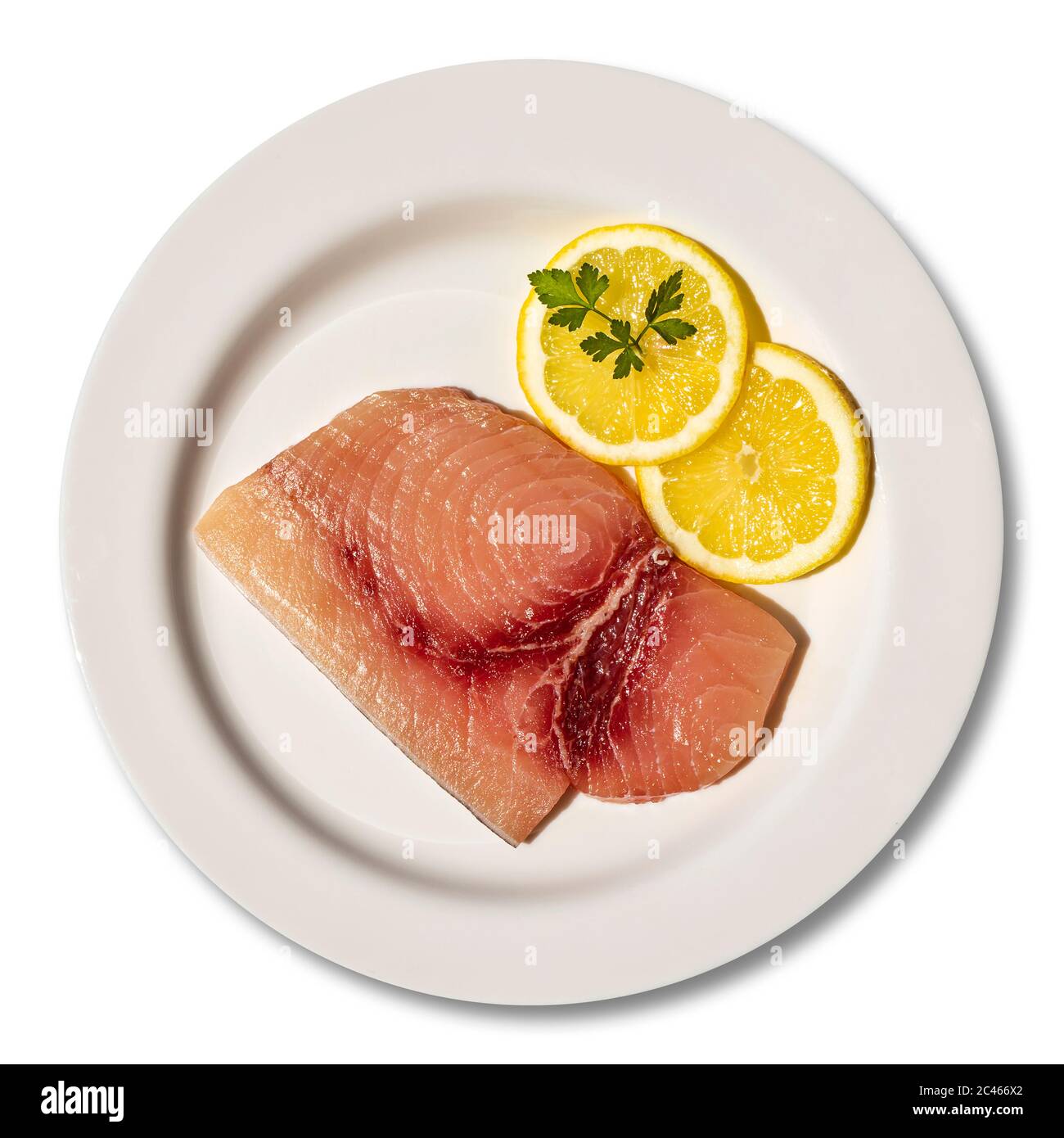 Macro close-up of a plate with a slice of raw, fresh swordfish. Dish garnished with two round slices of lemon and parsley leaf. Isolated on white back Stock Photo
