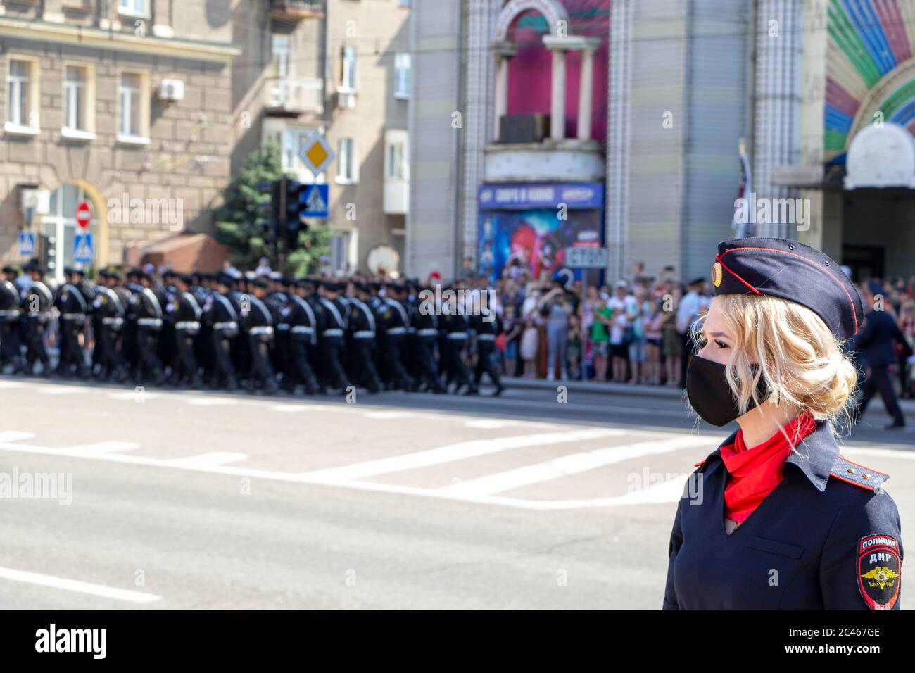 Donetsk, Donetsk People Republic - June 24, 2020: Policewoman in foreground in mask from coronavirus. Troops march along the main street of the city i Stock Photo