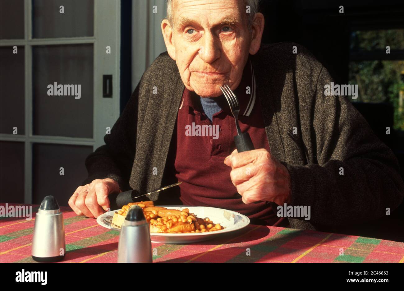 Old age pensioner eating baked beans and sausages for breakfast Stock Photo