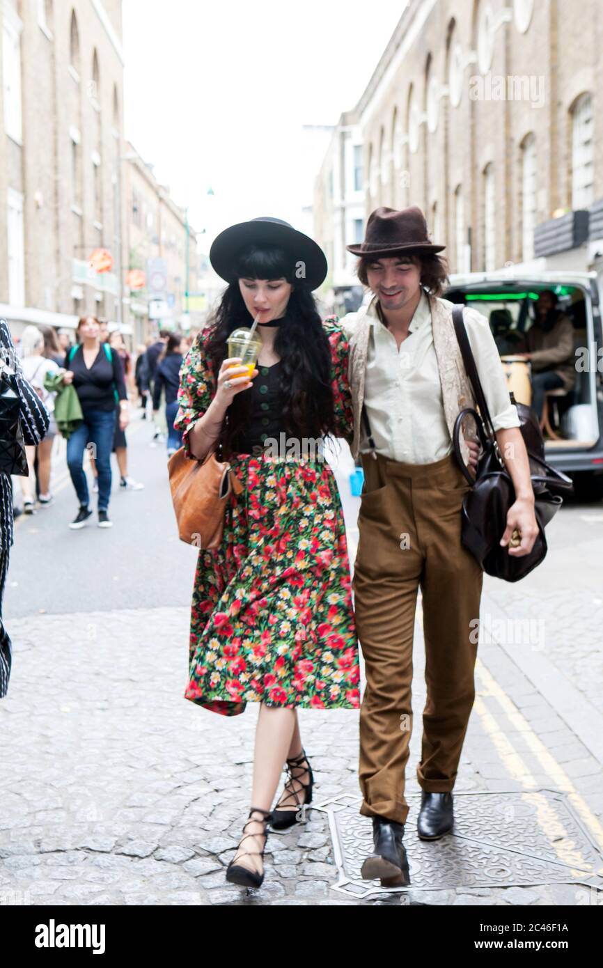 London, UK - 17 July 2019, Fashionably dressed man and woman walk along street. The man has white shirt and beige skinny pants and a hat. The woman is Stock Photo