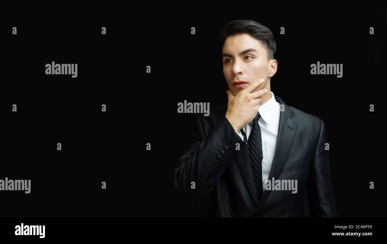 Young latin man in black suit, white shirt, black tie in thoughtful