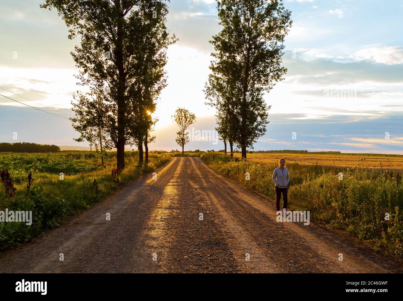Woman on a country road with the sun among the trees Stock Photo