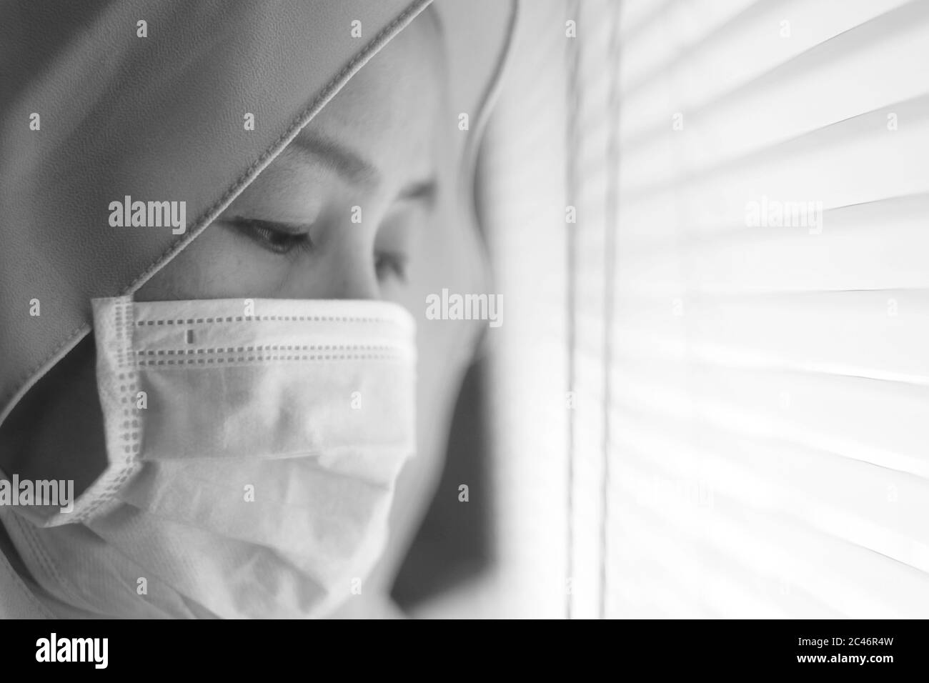 Sad woman in lockdown quarantine due to coronavirus covid 19 pandemic, looking trough window and crying, monochrome black white Stock Photo
