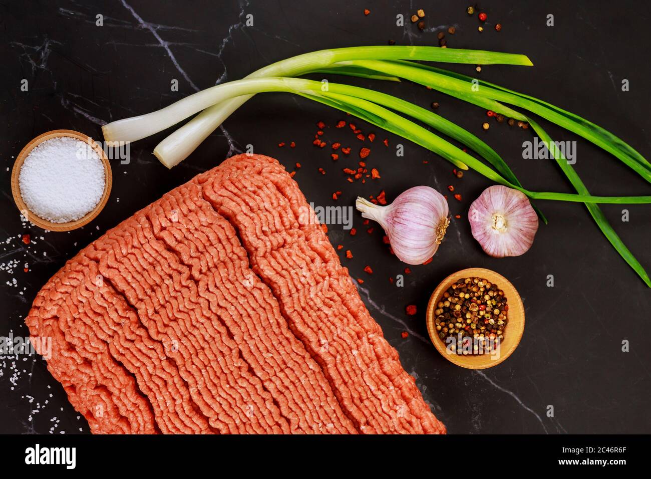 Uncooked ground beef with garlic and green onion on black background