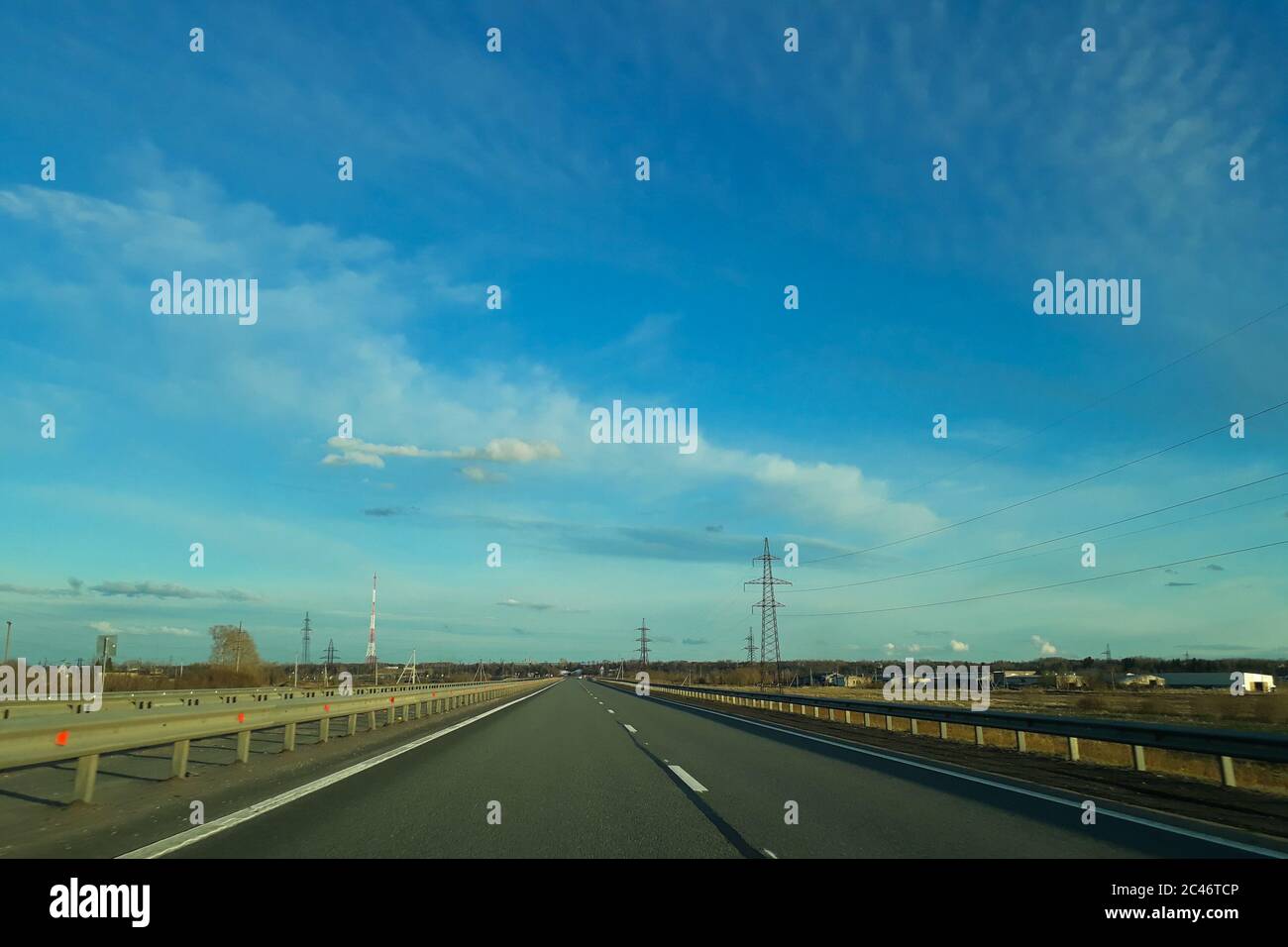 A road or highway leading to the horizon. View from the car window. Northern dim summer, blue sky with white clouds. Journey, the way home. Stock Photo