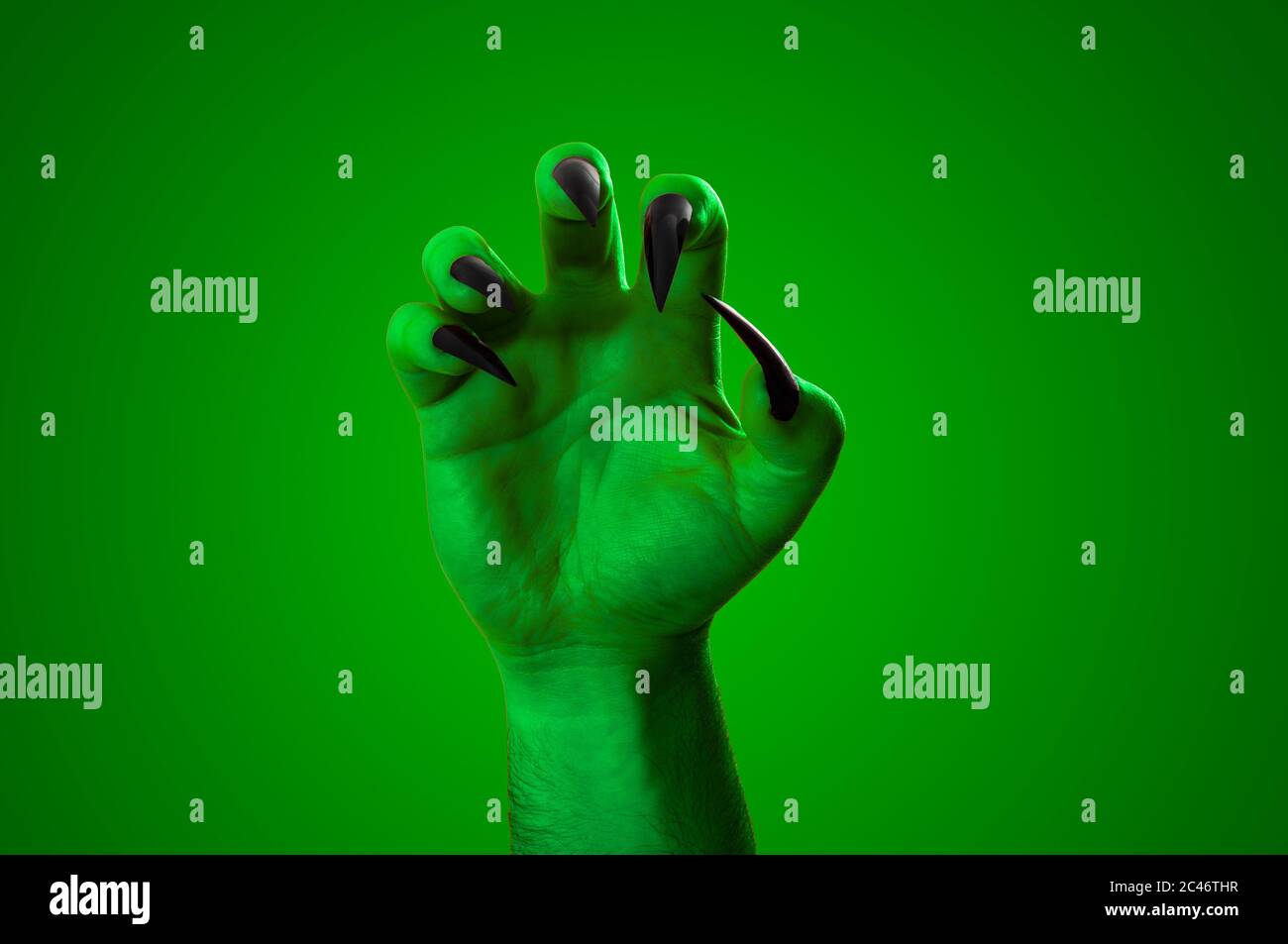 Halloween, nightmare creature and evil monster horror story concept with a scary zombie or demon hand with creepy long black nails isolated on green w Stock Photo