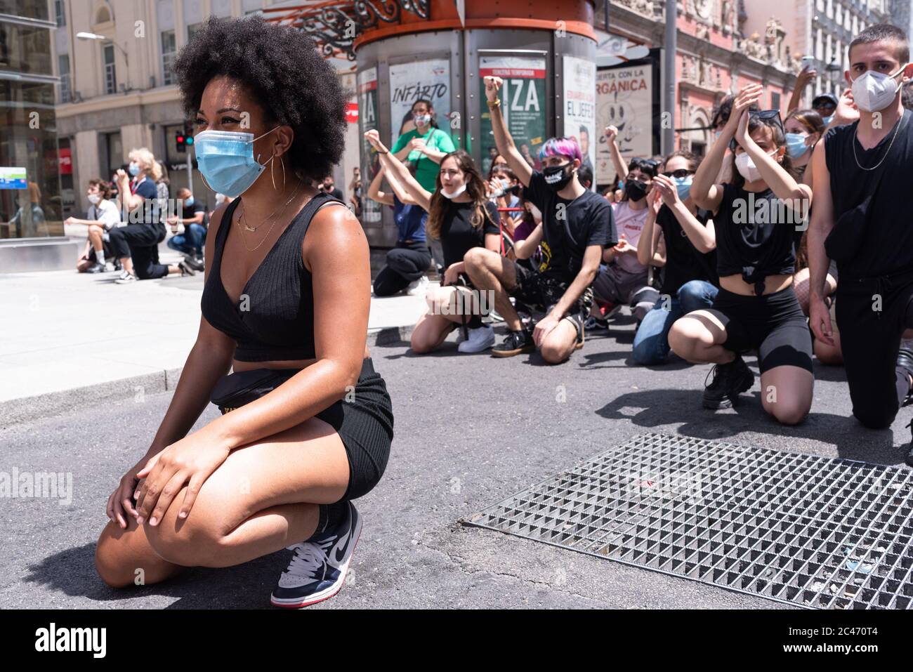 Black girl with mask kneeling in sign of protest in Calle de Alcalá. A group of white people supports her Stock Photo