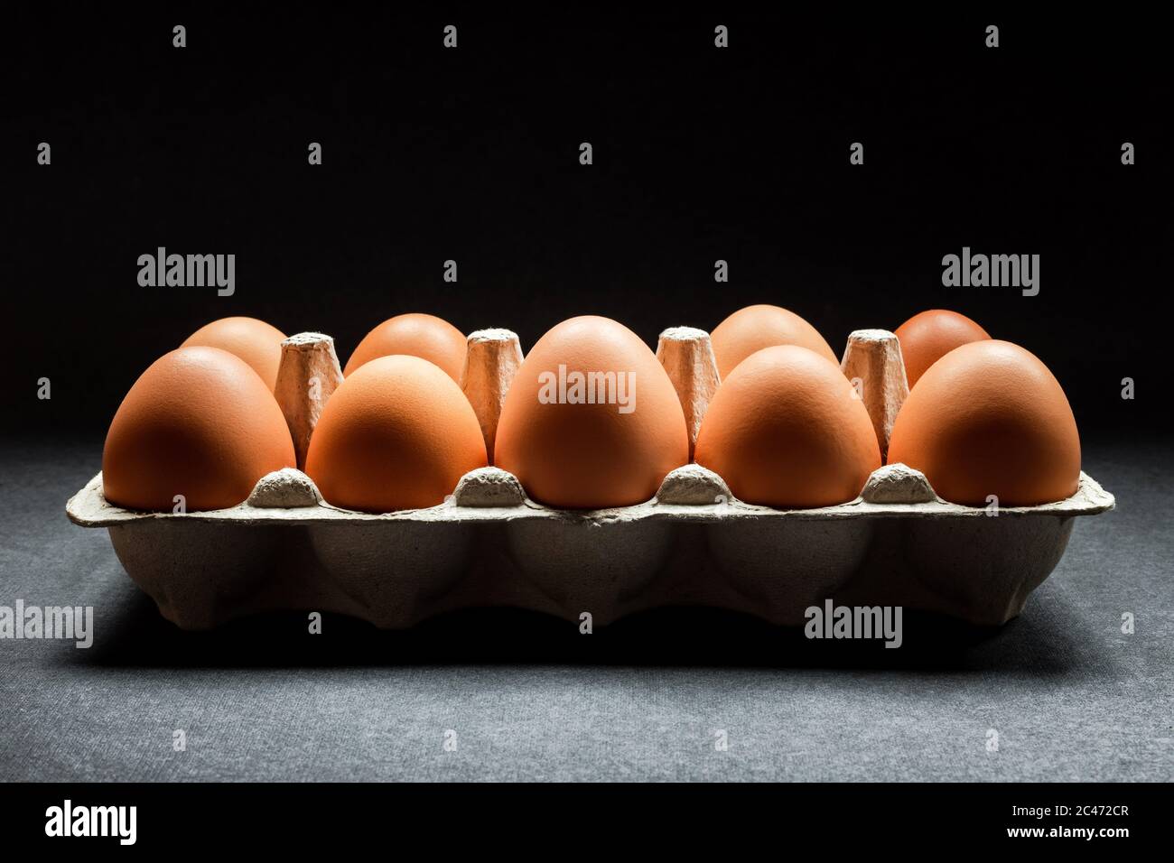 Chicken eggs in a carton on dark grey background, natural light coming from above, horizontal moody photo with deep shadows Stock Photo