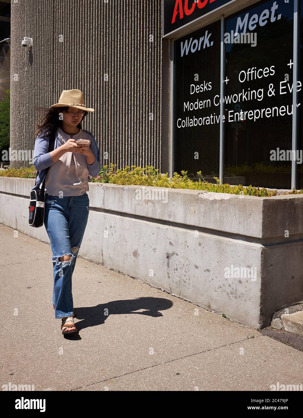 Trendy Young female walks the city streets texting on her cell phone while  wearing torn blue jeans and cowboy hat. St. Catharines, Ontario. June 2020  Stock Photo - Alamy