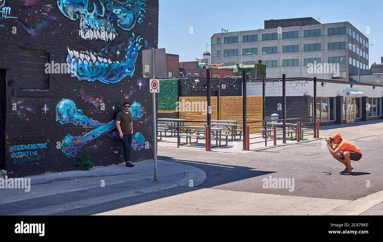 Photographer crouches in the street to take a photo of a restaurant worker taking a smoke break in a back alley with graffiti on the brick walls. Stock Photo