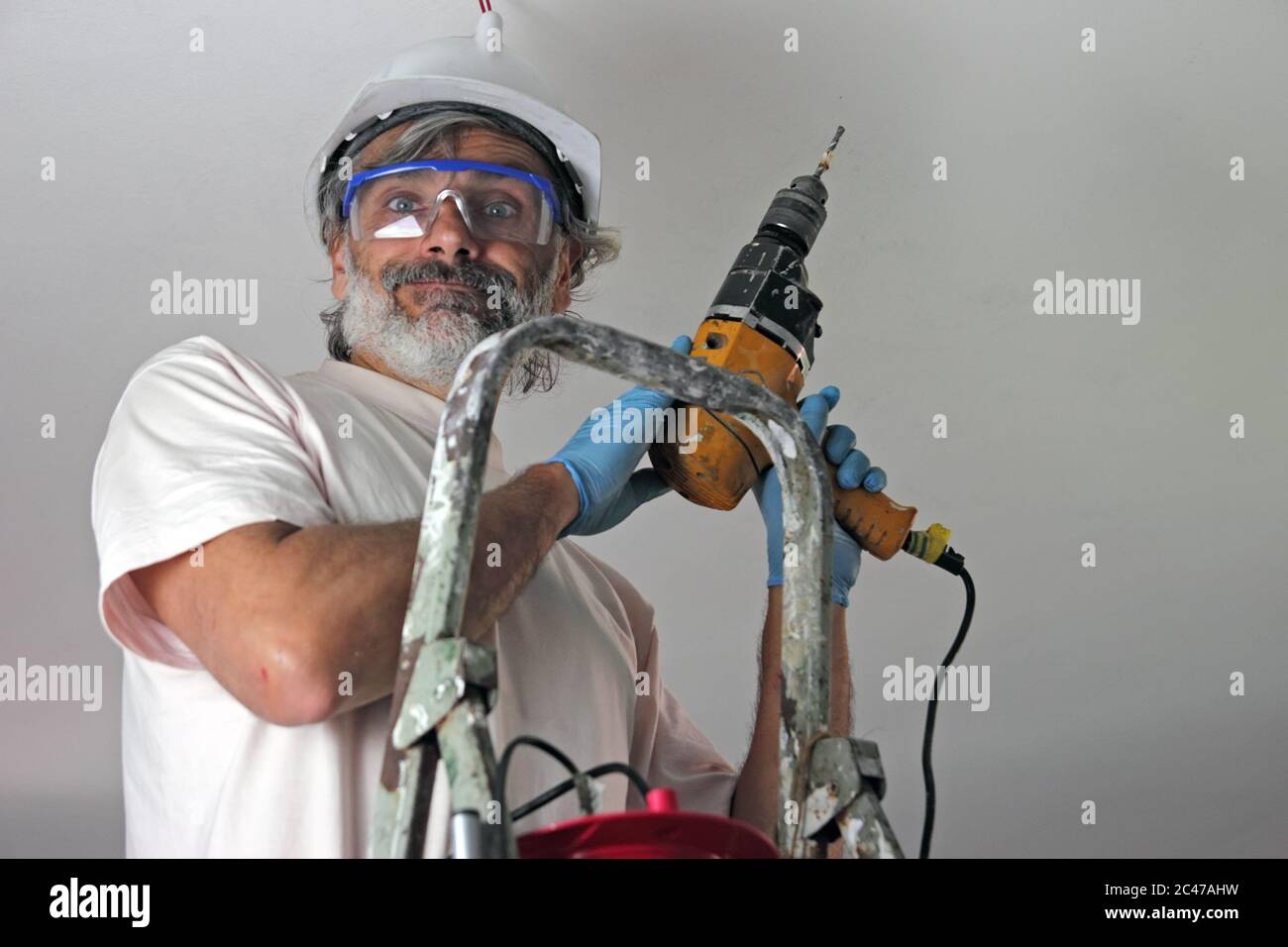 smiling man with electric drill  installing a lamp on the ceiling Stock Photo