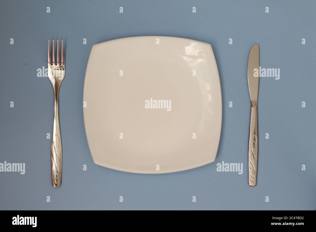 Empty plate, fork and knife over blue background. Clean plate and cutlery on light background. Top view. Flat lay. Stock Photo