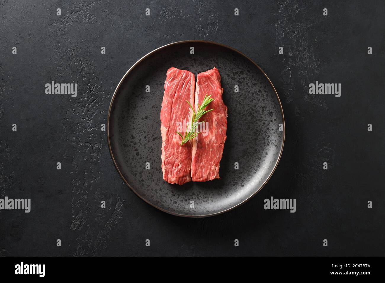 Raw ribeye steak on cutting board with rosemary on black background. Stock Photo