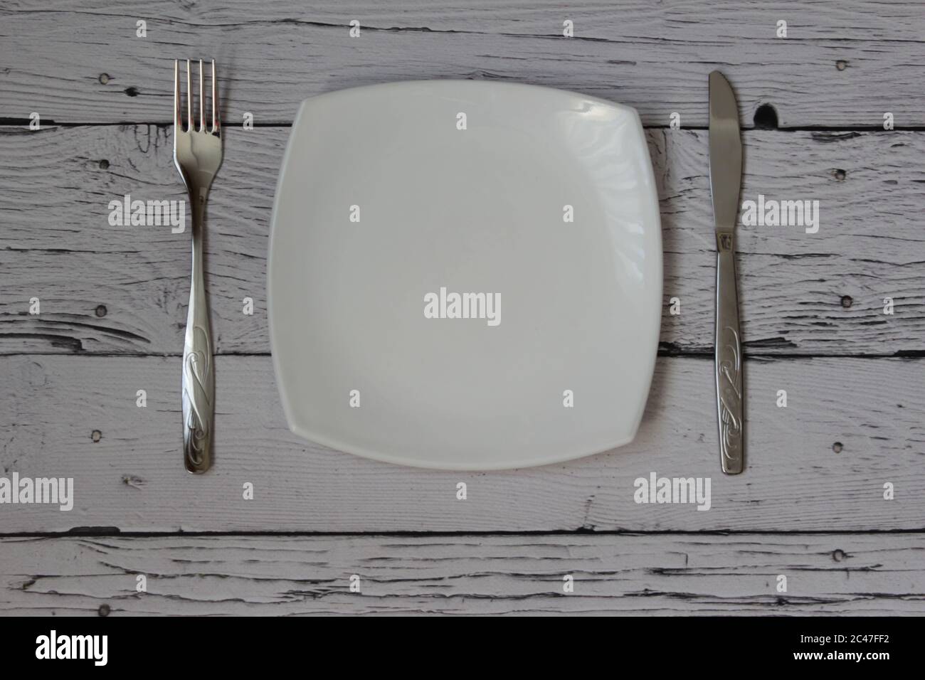 Empty plate, fork and knife over wooden background. Clean plate and cutlery on light background. Top view. Flat lay. Stock Photo