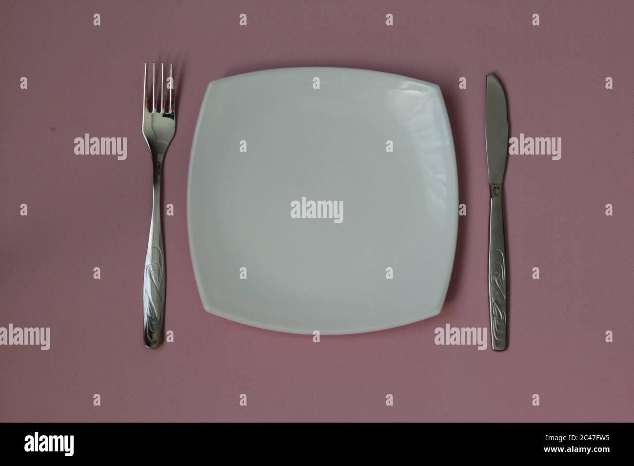 Empty plate, fork and knife over pink background. Clean plate and cutlery on light background. Top view. Flat lay. Stock Photo