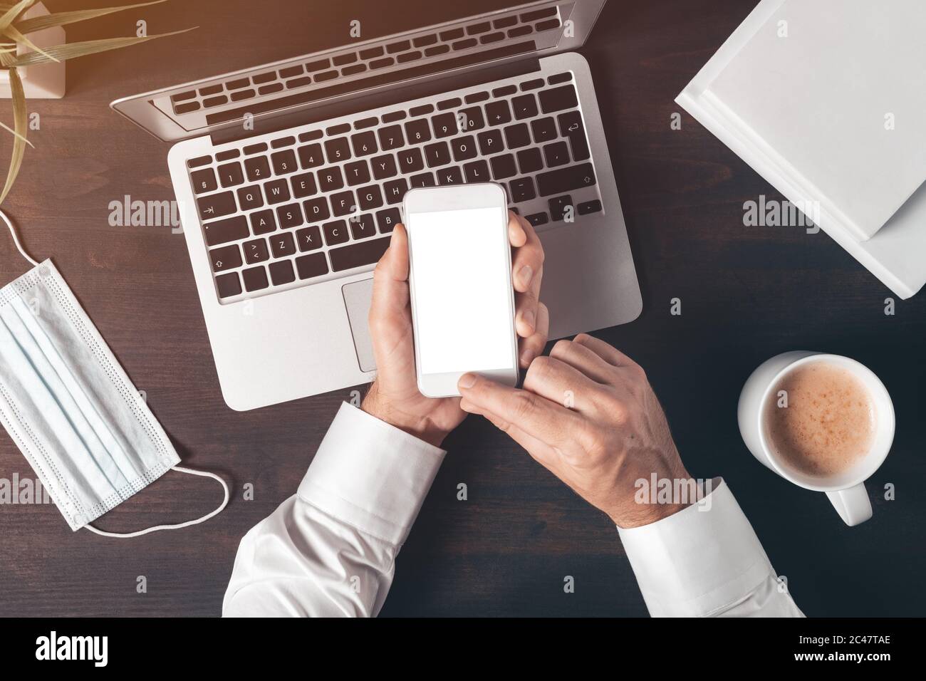 Mock up blank screen of modern smart phone in male hands over laptop computer, businessman using mobile phone, top view Stock Photo