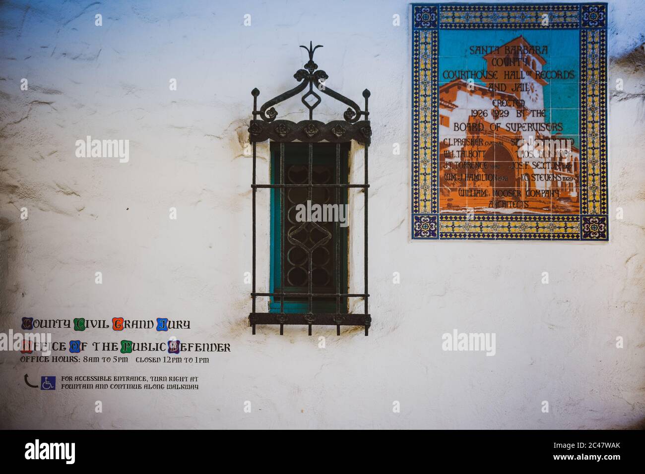 An outside vintage white wall of the Santa Barbara County Courthouse along with Spanish metal art window bars and pictorial tile signboard, erected in Stock Photo