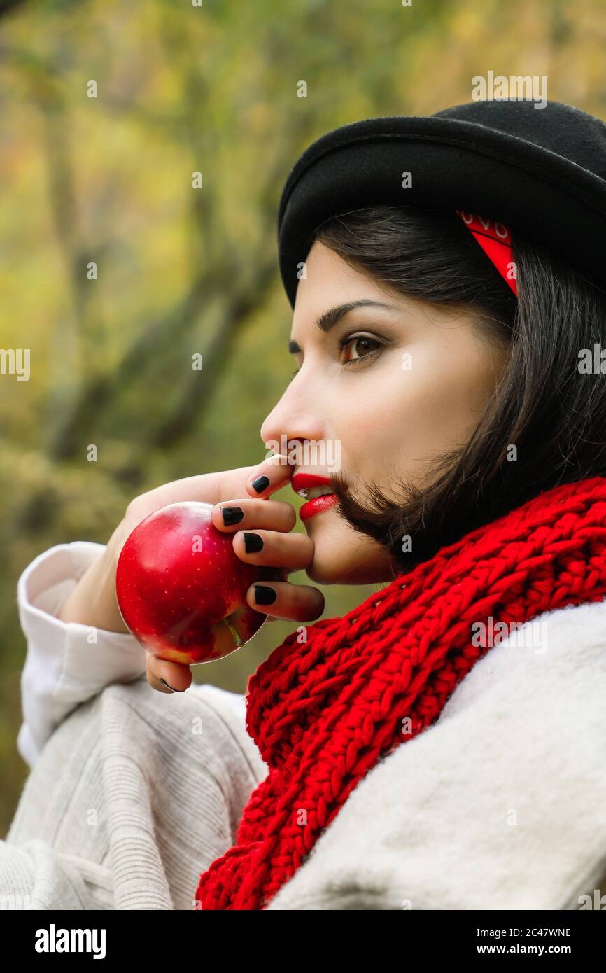 Beautiful woman in black hat and red scarf with a red apple in her hand. Autumn outdoor picnic Stock Photo