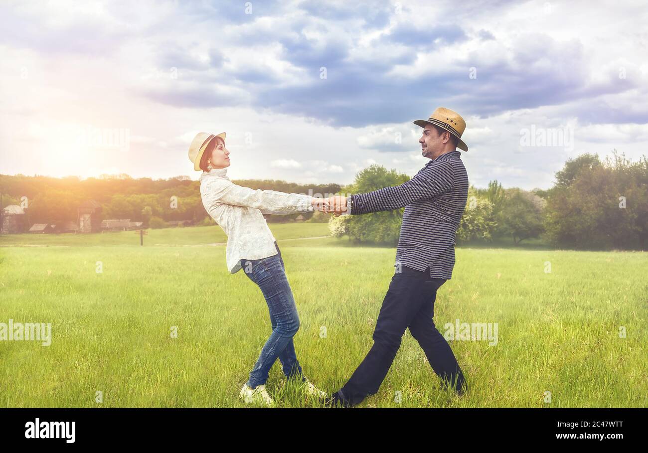 a portrait of a happy middle-aged couple holding hands in the green field. Stock Photo