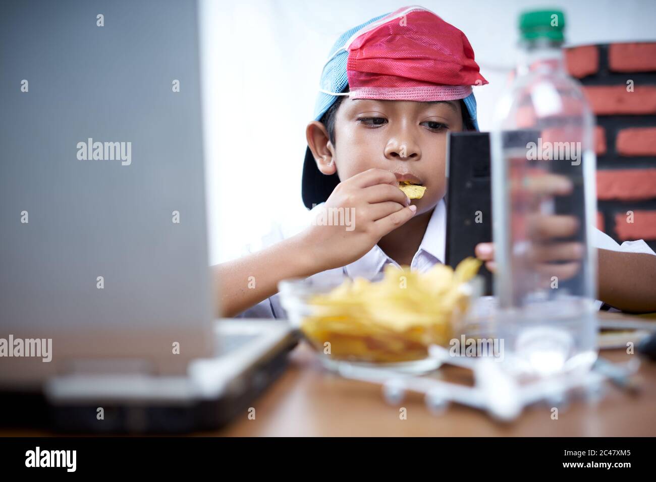 Young boy eating chips snack while study at home, New Normal Education concept Stock Photo