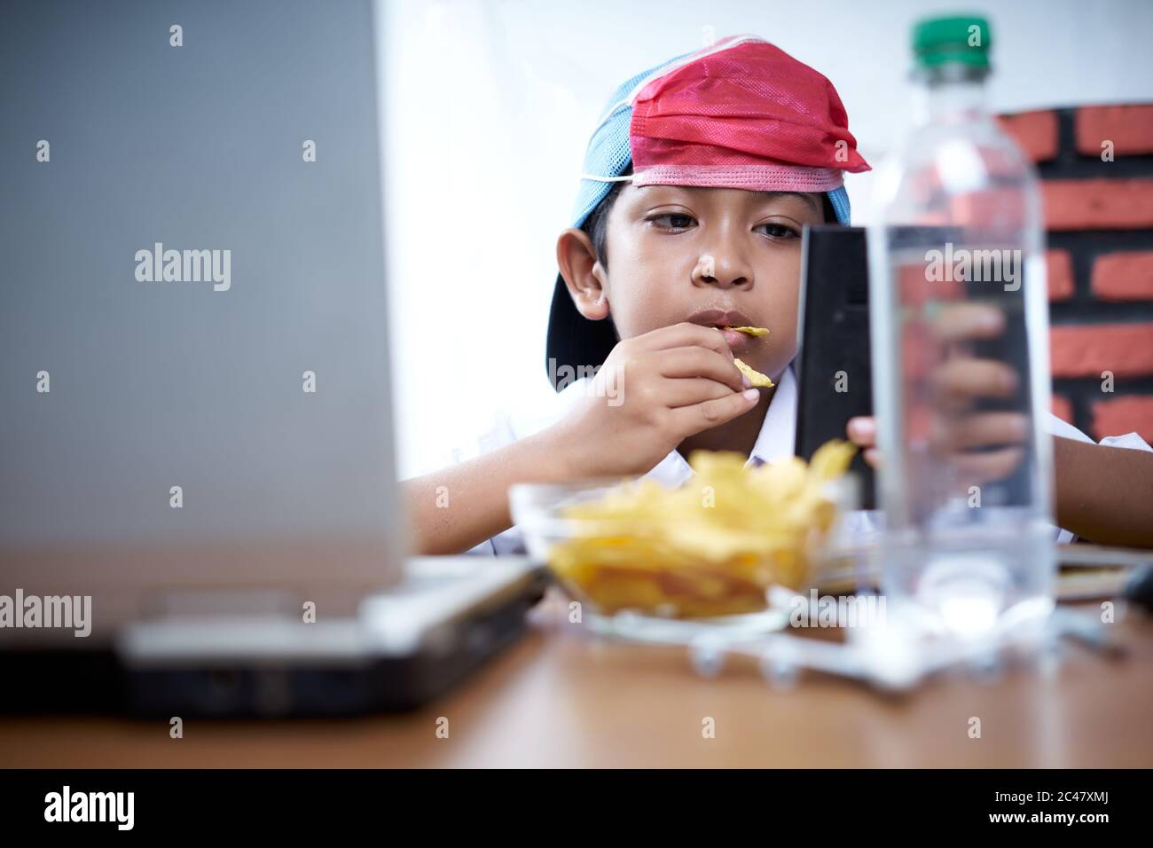 Young boy eating chips snack while study at home, New Normal Education concept Stock Photo