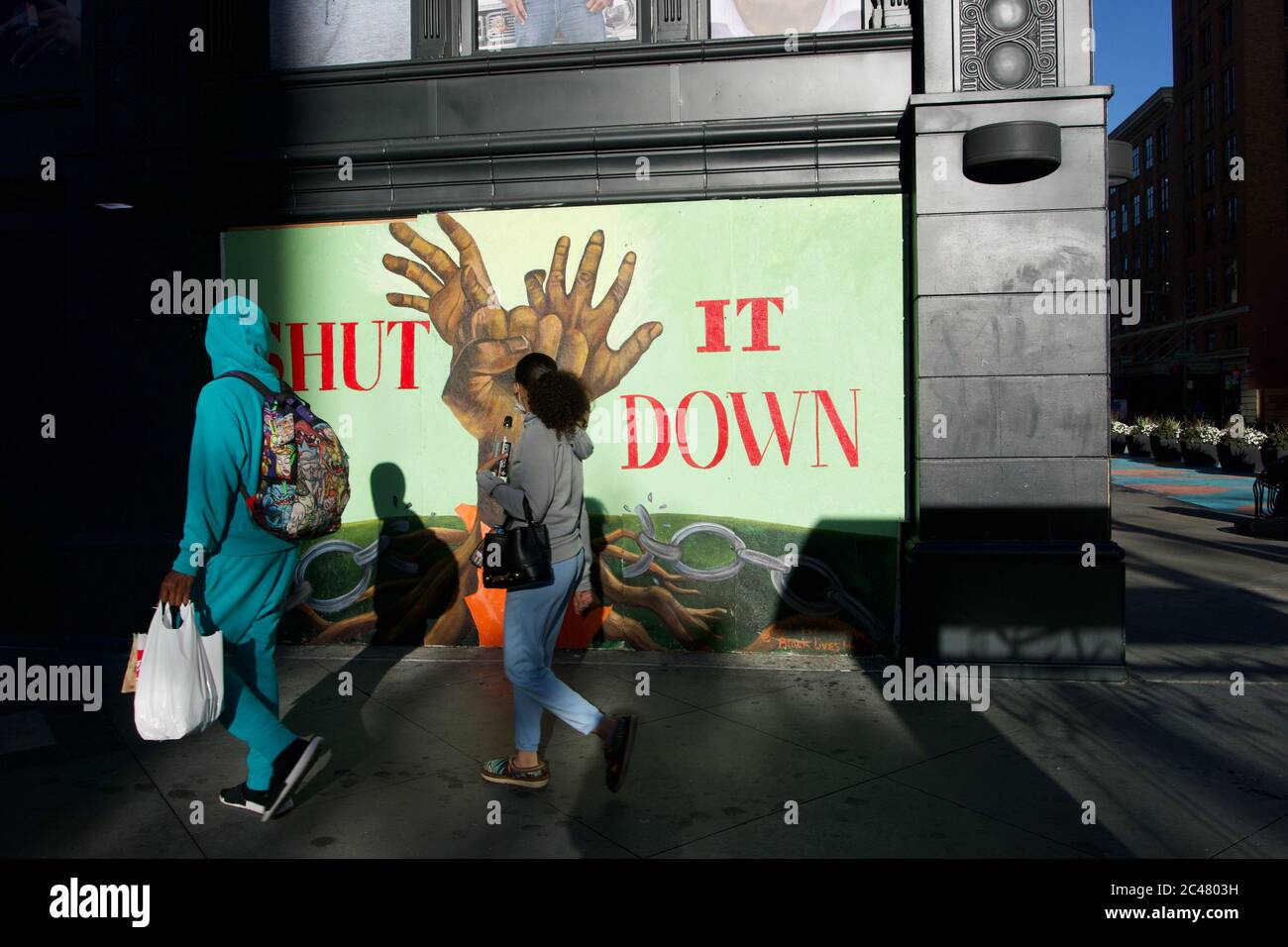 Pedestrians pass Black Lives Matter street art that says 'Shut It Down' on boarded up building after death of George Floyd. Downtown Oakland, CA, USA Stock Photo