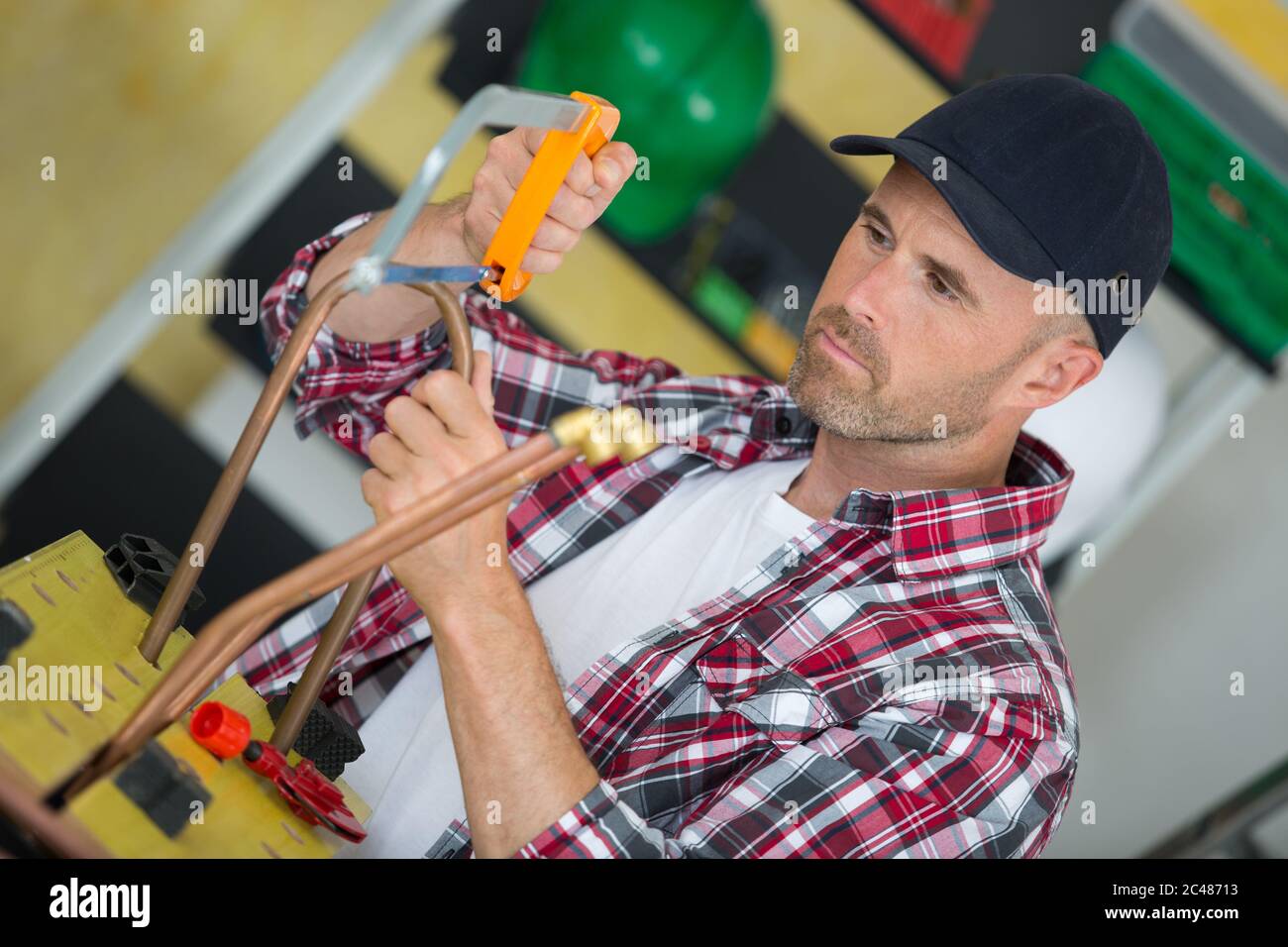man plumber using hacksaw to cut through copper pipe Stock Photo