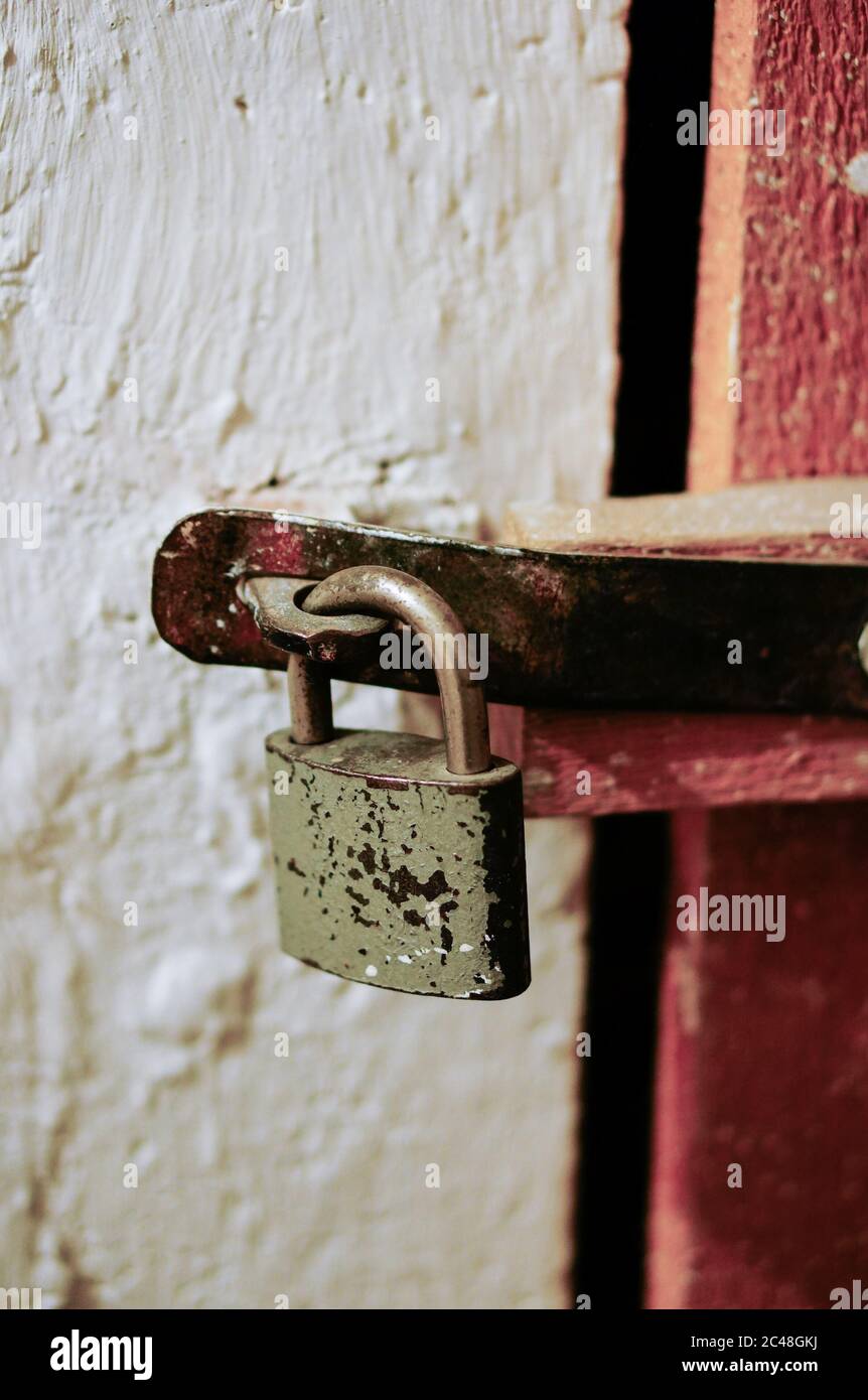 Vertical shot of an old rusty lock on a red door in a white wall ...