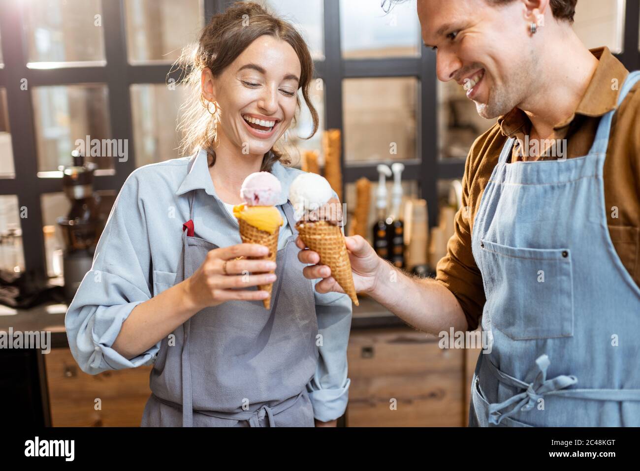 Two sellers cheering with yummy ice creams in waffle cone, having fun