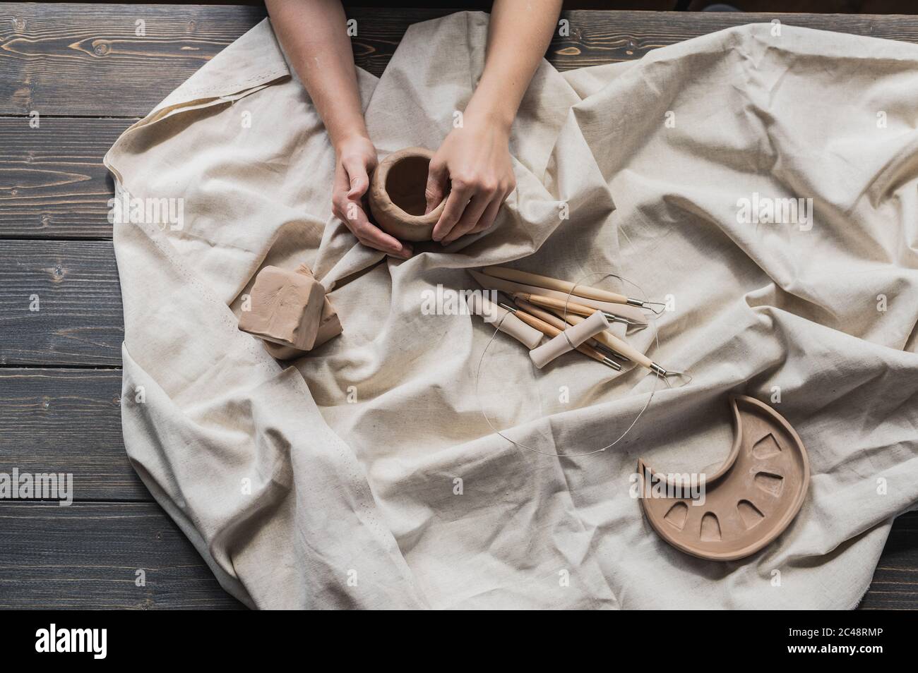 Female potters hand making clay pottery at the table with a different wooden tools close up. Stock Photo