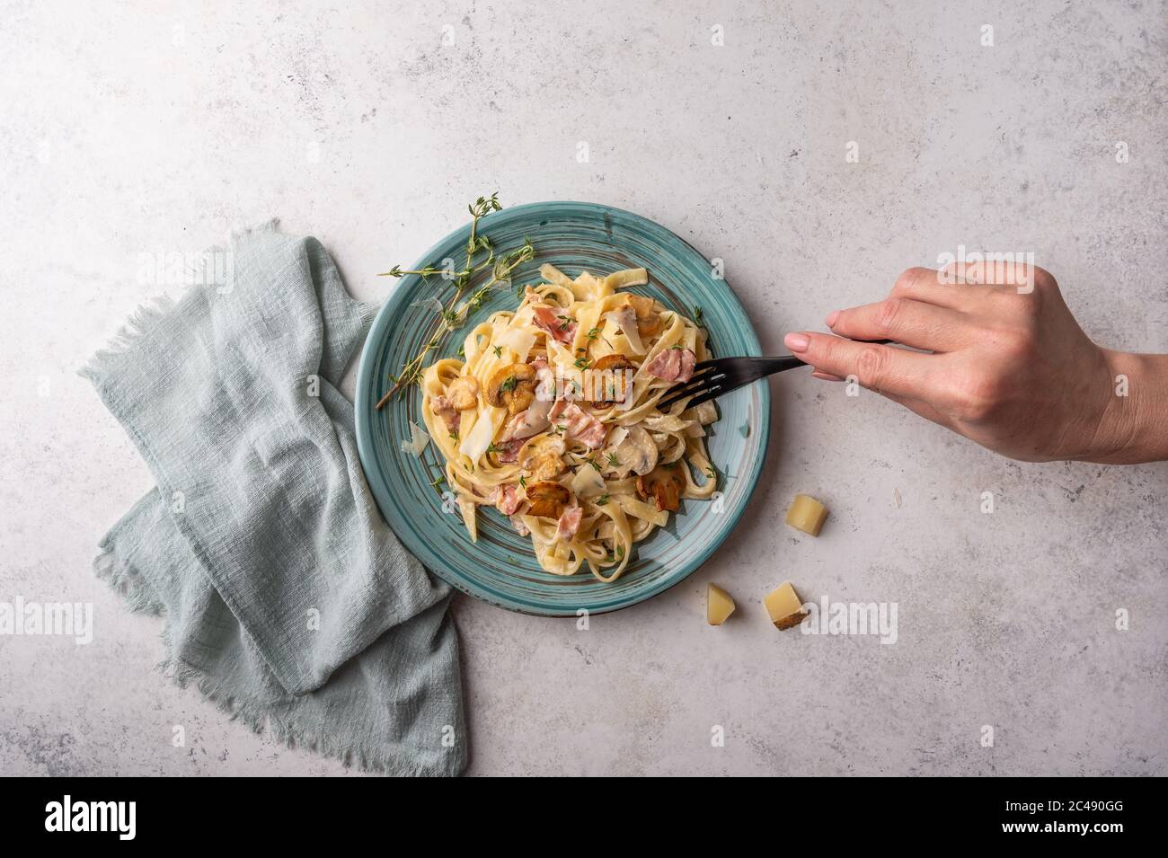 Woman's hand holds a fork with pasta fettuccine with mushrooms, bacon,  parmesan and bechamel sauce in plate on a light wooden background, top view  Stock Photo - Alamy