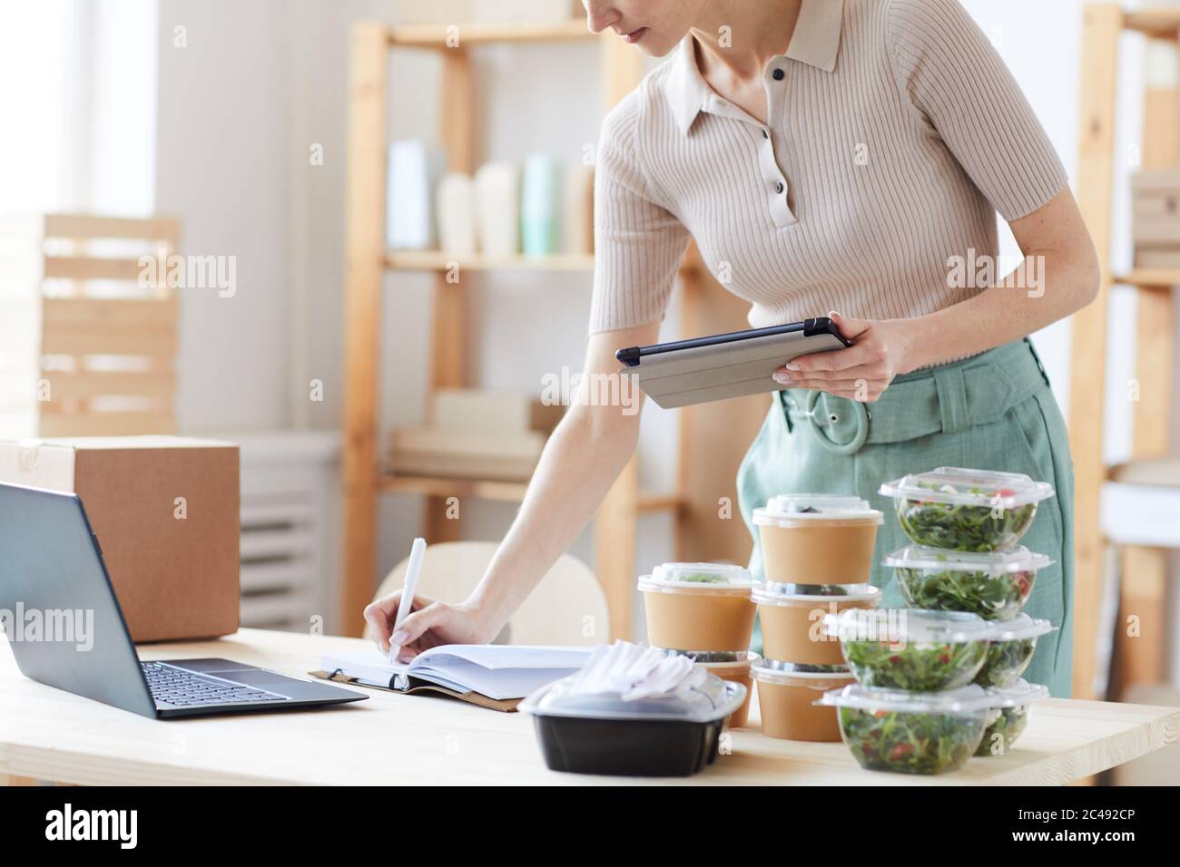Close-up of young woman using digital tablet and making notes in note pad she working in food delivery service Stock Photo