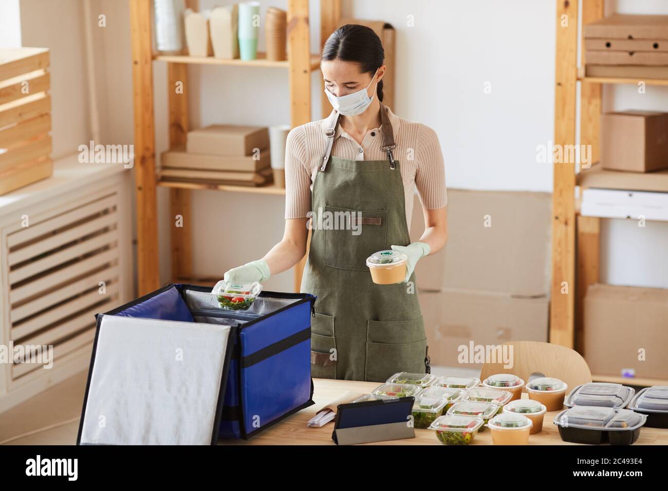 Young woman in protective mask packing food in big bag she working in ...